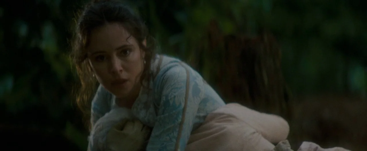 The Last of the Mohicans (1992) movie still: medium — A dense forest environment with thick foliage and a dark tree stump in back. A young woman…
