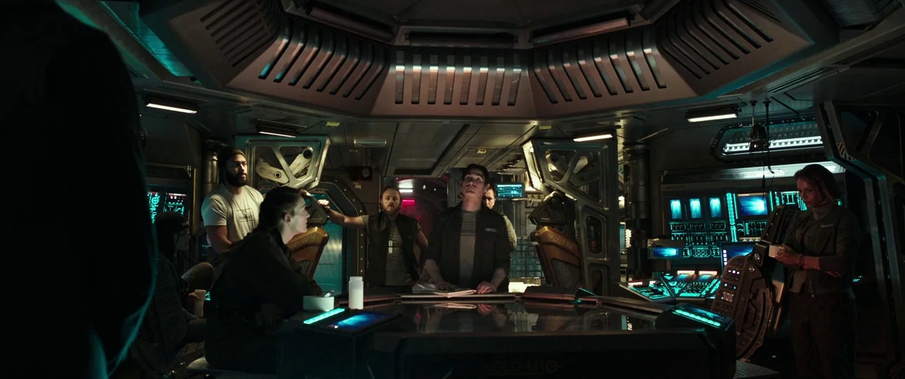 Alien: Covenant (2017) movie still: wide — A dimly lit industrial spaceship command deck features a large central holographic table display. Several…