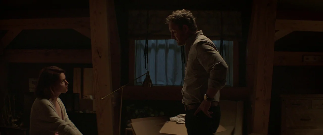 Pet Sematary (2019) movie still: medium — A dark attic features exposed wooden beams and a small window with heavy curtains. A man stands while a…