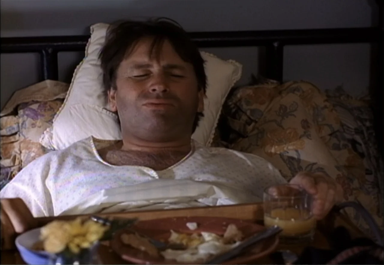 Chance of a Lifetime (1998) movie still: medium — A man lies in a bed with floral pillows and a headboard. He rests in the bed with his eyes closed…
