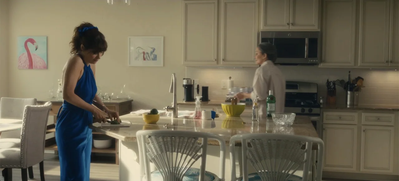 Merv (2025) movie still: medium — A well-lit contemporary home space features white cabinets and a polished stone island surface. Two women stand in…