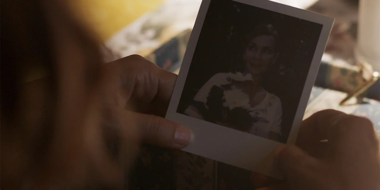 Demonic (2015) movie still: closeup — An interior space features patterned fabric surfaces in soft, muted natural light. A pair of hands holds a…