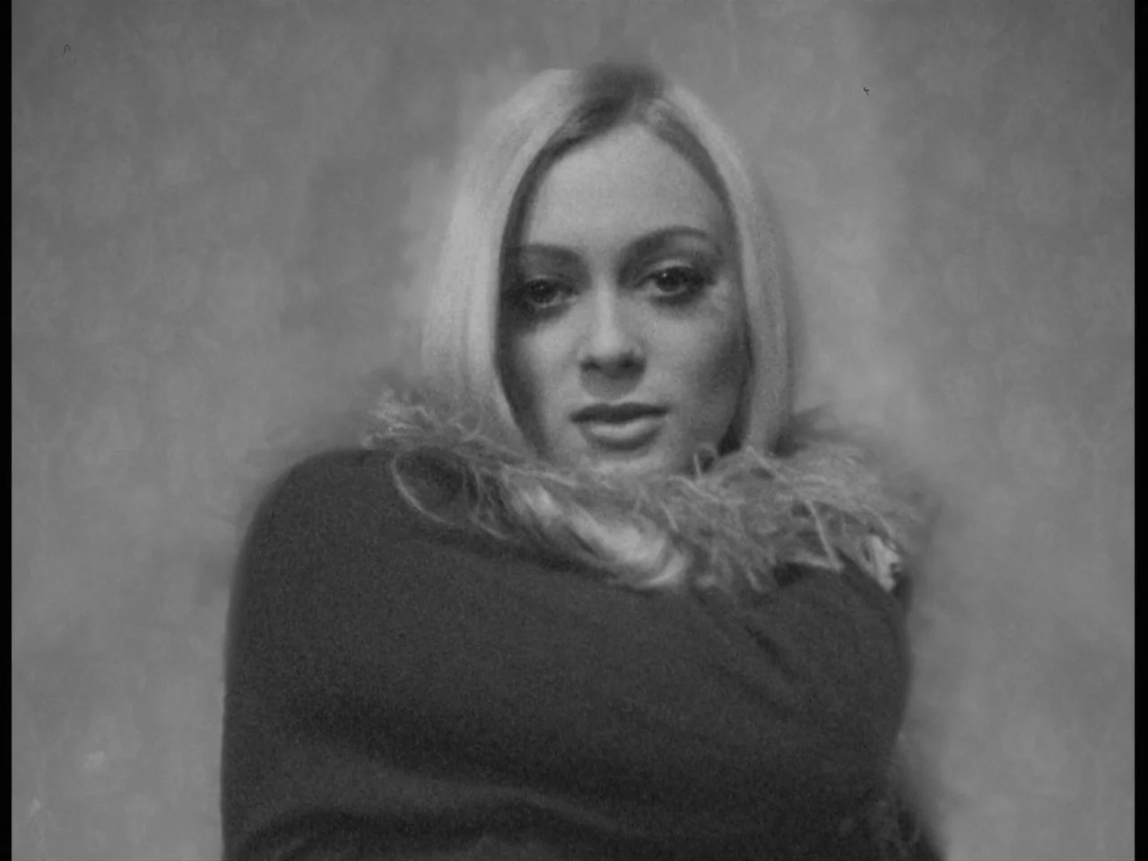 A Woman Kills (1968) movie still: closeup — A woman stands before a textured, patterned wall surface. The subject gazes directly toward the viewer…