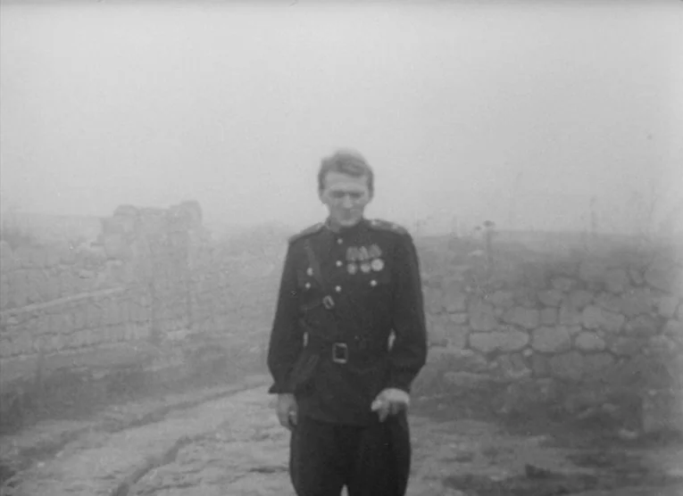 Wings (1966) movie still: fullbody — A man in a military uniform stands in front of ancient stone ruins. Dense fog obscures the surrounding…