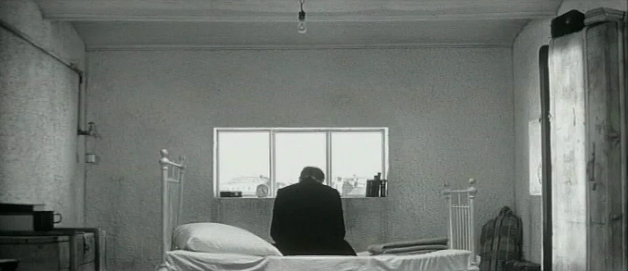 And The Fifth Horseman is Fear (1965) movie still: wide — A stark room features plain light-colored walls and a bare ceiling fixture. A man wearing…