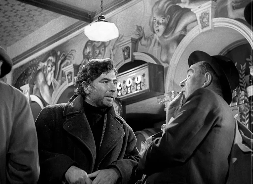 Odd Man Out (1947) movie still: medium — A dark pub interior features wall murals of figures and an overhead pendant lamp. Two men stand close…