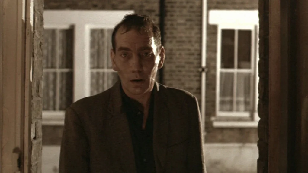 Distant Voices, Still Lives (1988) movie still: medium — A man stands in an exterior doorway at night against a brick wall. The building features…