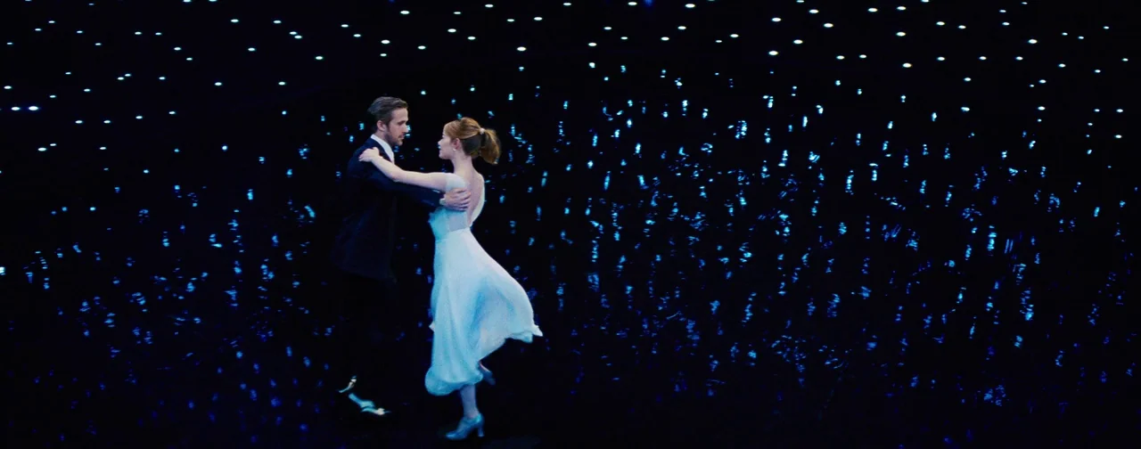 La La Land (2016) movie still: fullbody — A dark, expansive planetarium interior filled with glowing projected stars against a pitch-black…