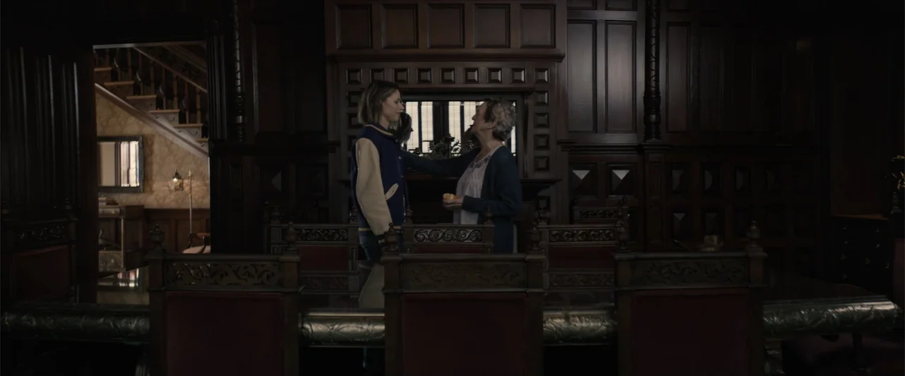 Equation of Love and Tone Deafness (2015) movie still: medium — A dark, wood-paneled dining room features an ornate dark wooden fireplace and long…