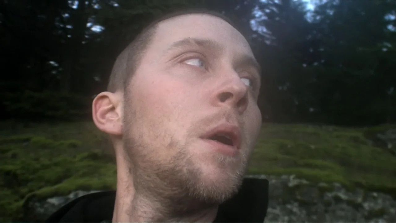 Daniel (1983) movie still: closeup — A mossy, forested outdoor area is visible behind the man's head. A man with a short haircut looks off-screen…