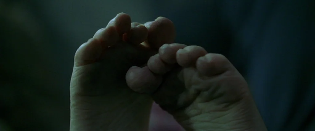 Panic Room (2002) movie still: closeup — A dimly lit room provides a dark background for the pale, exposed feet. Two feet rest against each other…