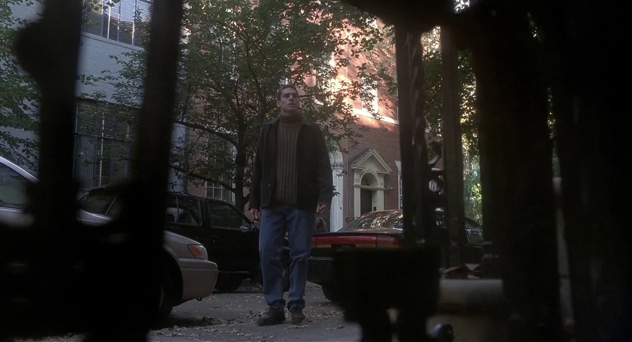 The Sixth Sense (1999) movie still: fullbody — A man stands on an asphalt residential street lined with brick row houses and trees. The man looks up…