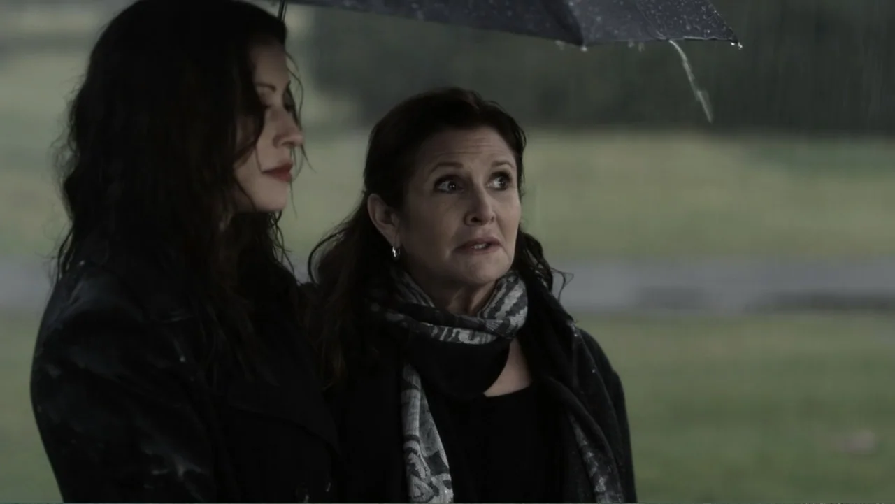 It's Christmas, Carol! (2012) movie still: medium — Two women stand outdoors on a rainy day under a black umbrella. The figures are positioned…