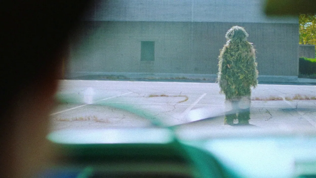 Strawberry Mansion (2021) movie still: wide — A vast, cracked asphalt parking lot sits before a featureless, light gray concrete wall. A person…