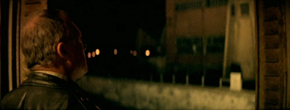 I Stand Alone (Seul Contre Tous) (1998) movie still: medium — A man in a leather jacket stands inside a dimly lit space near a window. He observes a…