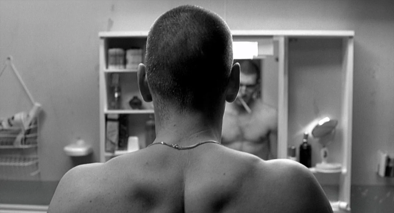 La Haine (1995) movie still: medium — A spartan bathroom with a wall-mounted medicine cabinet and various toiletries on glass shelves. A shirtless…