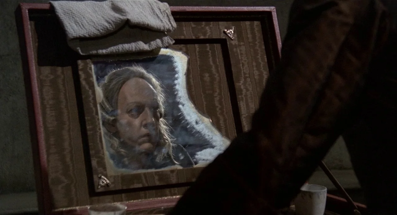 Fellini’s Casanova (1976) movie still: medium — A man's face is reflected in a wooden-framed mirror propped up on a surface. A white towel is draped…
