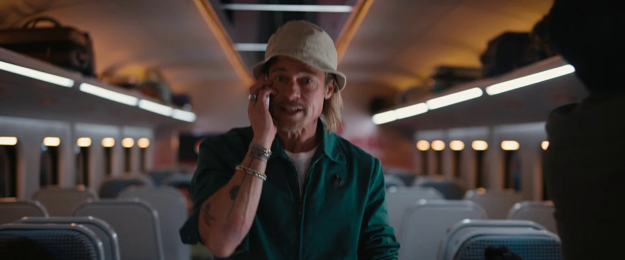 Bullet Train (2022) movie still: medium — The interior of a modern passenger train carriage features rows of empty blue seats. A man in a bucket hat…
