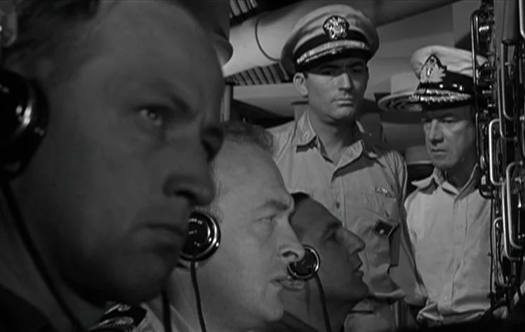 On The Beach (1959) movie still: medium — Four men in military uniforms work in the tight, crowded quarters of a submarine. The officers monitor…