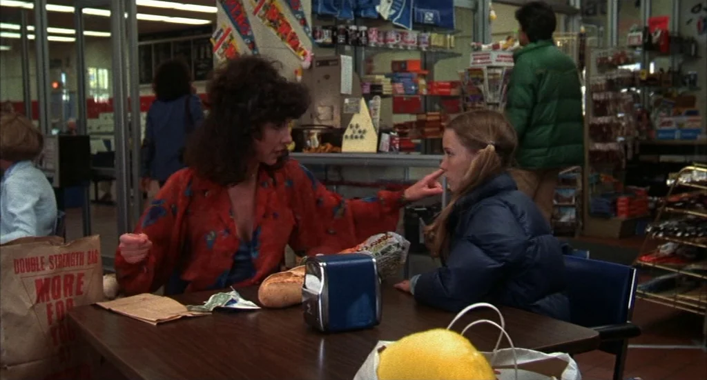 Melvin & Howard (1980) movie still: medium — A well-lit convenience store interior with shelves stocked with various packaged goods. A woman in a…