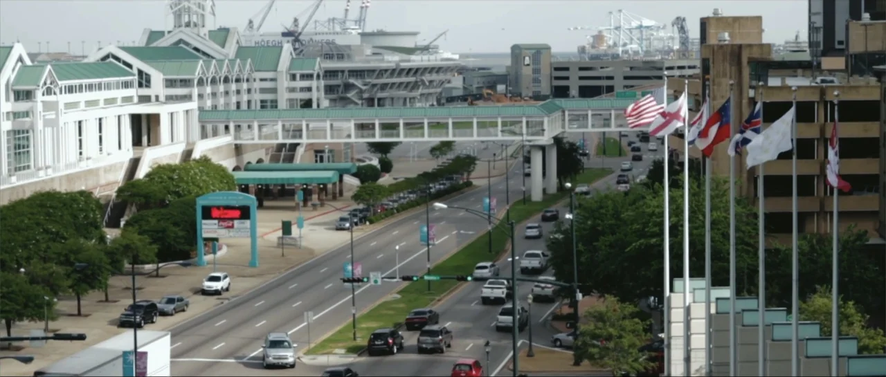 Rage (2014) movie still: establishing — A wide view shows a modern city street beside a large multi-building convention complex. Numerous cars…