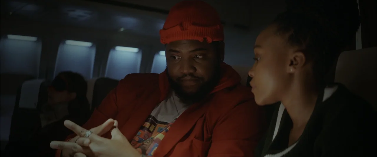 A Scam Called Love (2025) movie still: medium — The interior of a darkened airplane cabin with illuminated rows of overhead window panels. A man in…