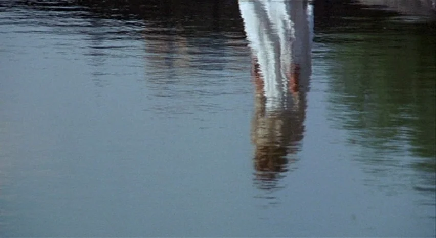 A Safe Place (1971) movie still: establishing — A calm expanse of water fills the frame with gentle ripples on the surface. A distorted reflection…