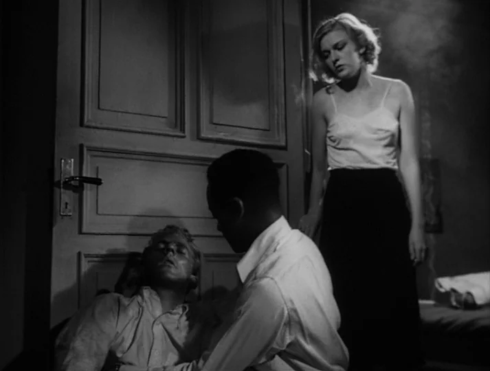 Port of Call (1948) movie still: medium — An interior space features a wooden door with panels against a plain wall. A man supports an unconscious…