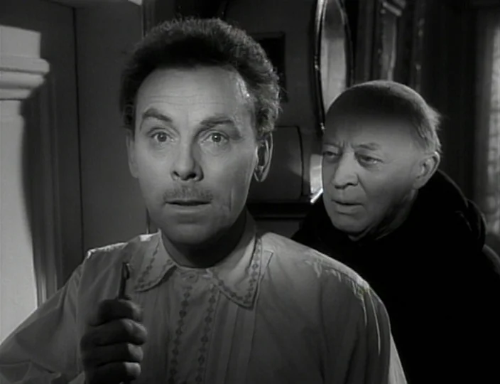 The Devil’s Eye (1960) movie still: medium — Two men stand closely together in a dimly lit interior room at night. The foreground man clutches a…