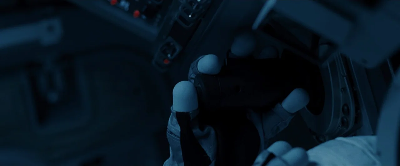 Ad Astra (2019) movie still: closeup — A dark, cramped control cockpit features various technical switches and backlit instrument panels. A gloved…