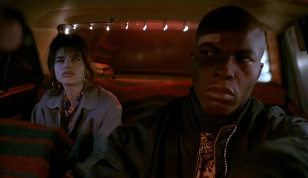 Night on Earth (1991) movie still: medium — The interior of a car at night features dark patterned upholstery and small lights. A man with a bandage…