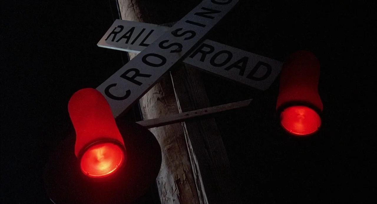 Mississippi Burning (1988) movie still: closeup — A dark railroad crossing sign is mounted on a wooden utility pole. Two red circular signal lights…