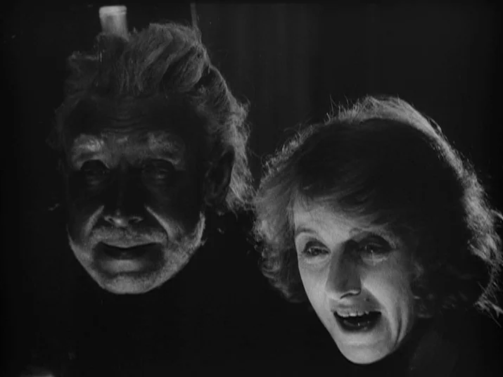 Making of: The Wheel (La Roue) (1923) movie still: medium — A dark, unidentifiable space where faces emerge from deep shadows. Two people gaze at an…
