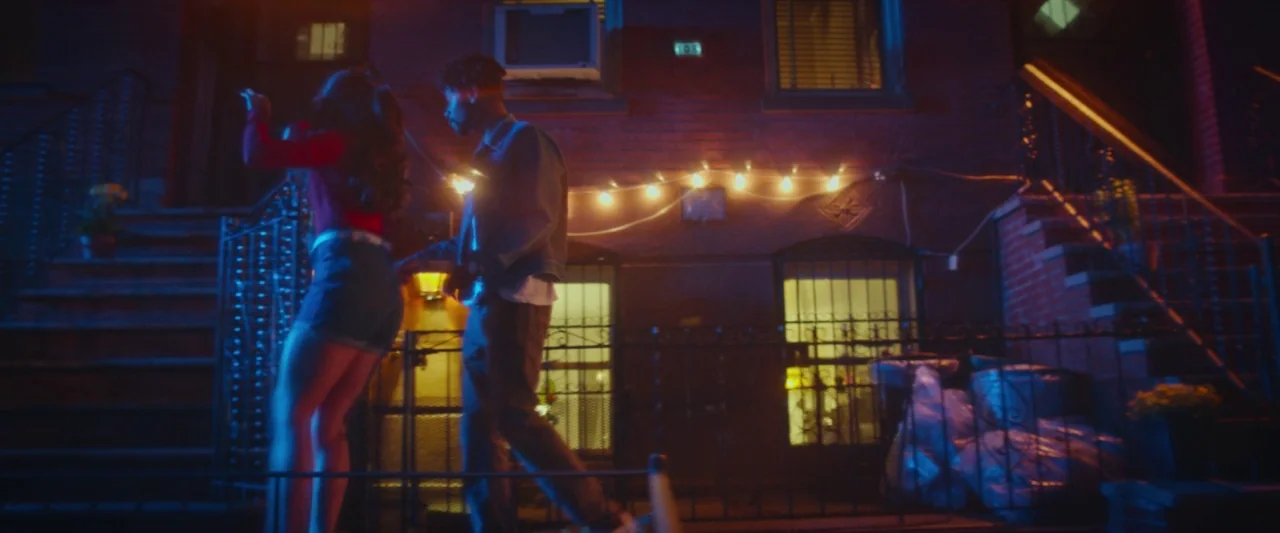 Someone Great (2019) movie still: fullbody — A brick residential building at night features string lights draped across its facade. A man and woman…
