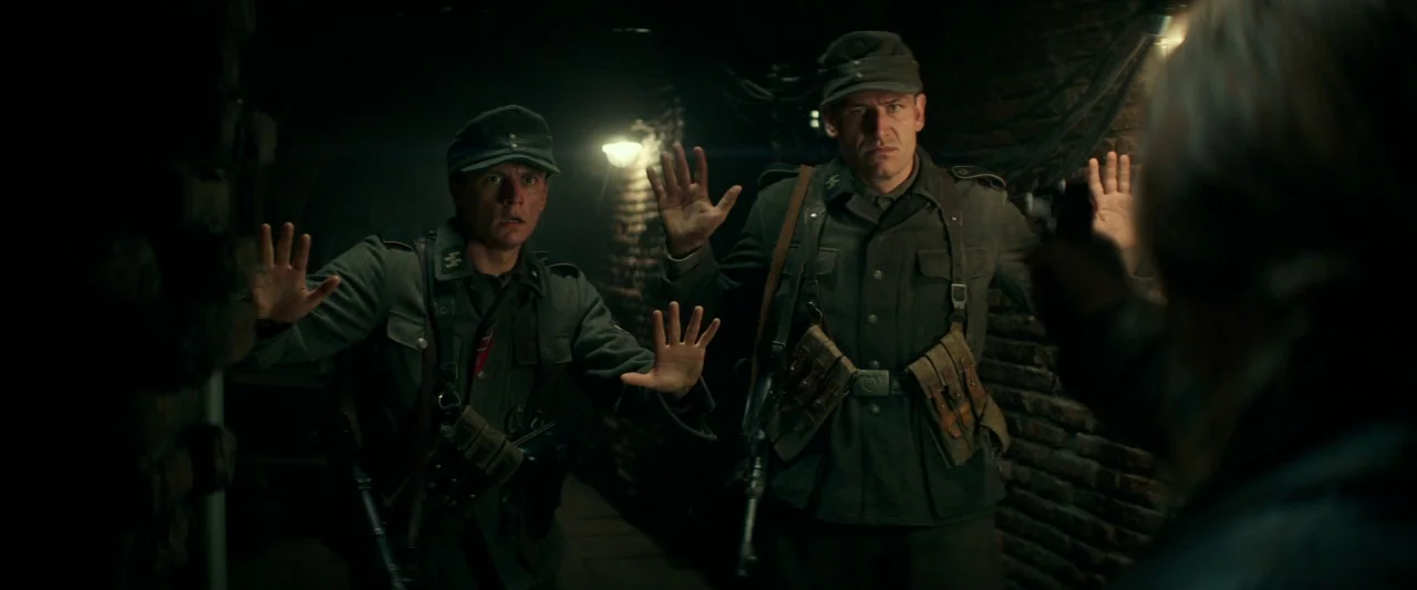 Overlord (2018) movie still: medium — A dark subterranean tunnel made of brick and stone features low hanging exposed wires. Two soldiers in period…