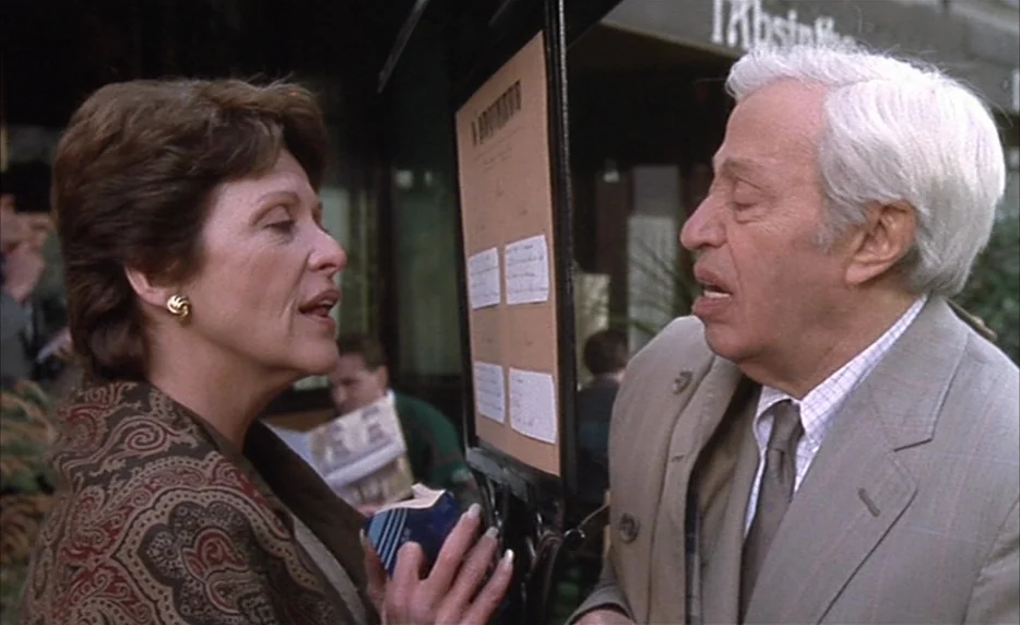 I Want To Go Home (1989) movie still: medium — A woman and an older man stand at an outdoor cafe reading a menu board. They engage in conversation…