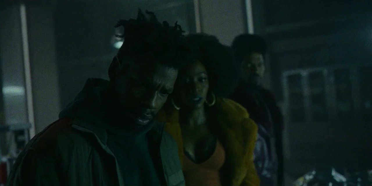 They Cloned Tyrone (2023) movie still: medium — A dimly lit industrial space with tiled walls and metallic structural supports. Three individuals…