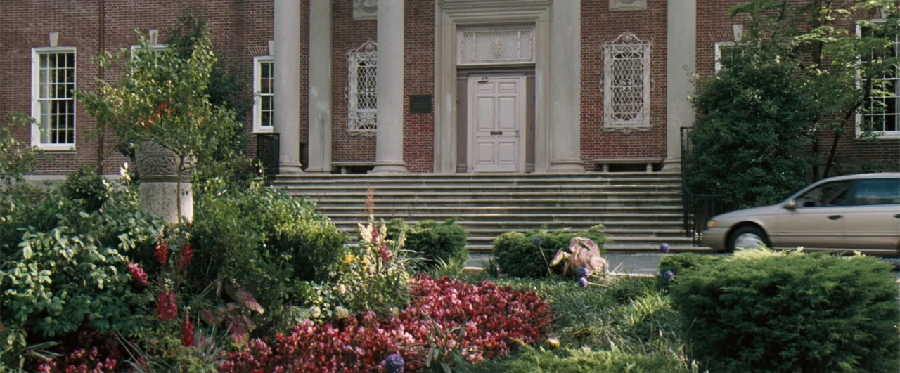 The Pelican Brief (1993) movie still: establishing — A red brick academic building with white columns features a grand entrance with stairs. The…