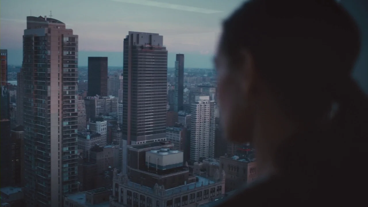 Margin Call (2011) movie still: medium — A high-rise room overlooks a dense city skyline during the fading light of dusk. A person seen from behind…