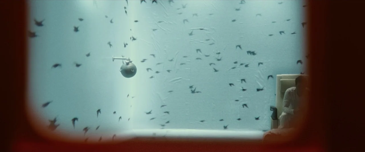 Ad Astra (2019) movie still: wide — A stark white interior space contains a dark spherical object and numerous small black shapes. A person sits in…