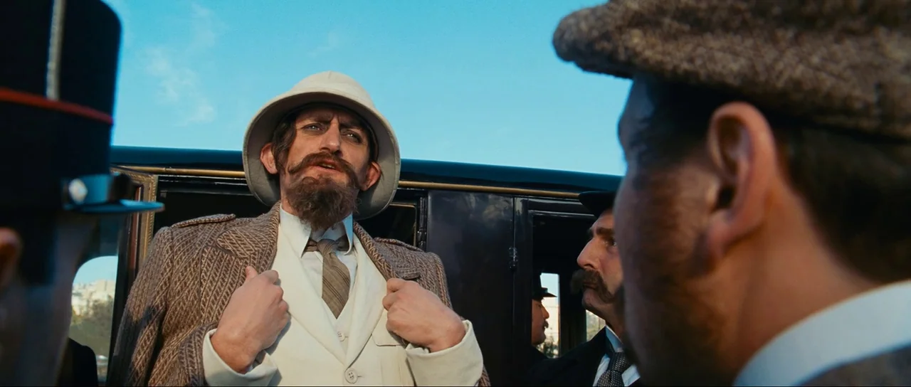 The Extraordinary Adventures of Adèle Blanc-Sec (2010) movie still: medium — An outdoor scene features a man in a pith helmet surrounded by other…