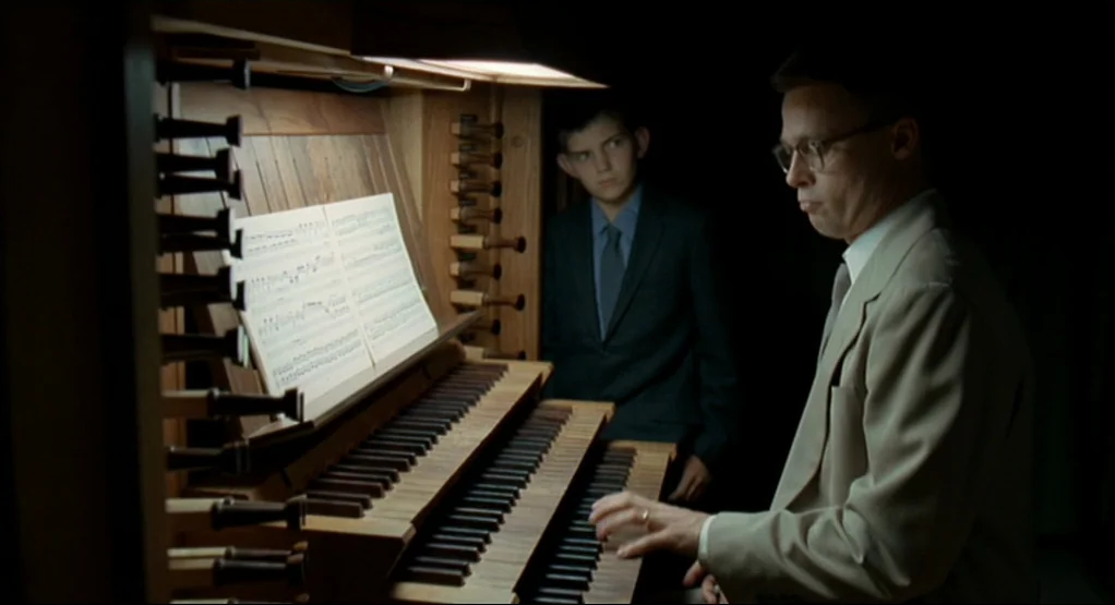 The Tree Of Life (2011) movie still: medium — A pipe organ console featuring multiple wooden manuals and rows of drawknobs. A man in a suit plays…