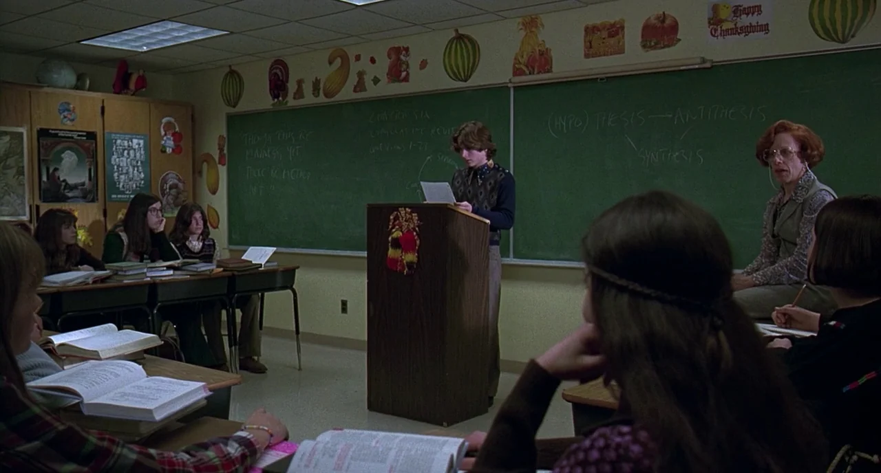 The Ice Storm (1997) movie still: wide — A 1970s school setting with Thanksgiving decorations and notes written on a chalkboard. A male student…