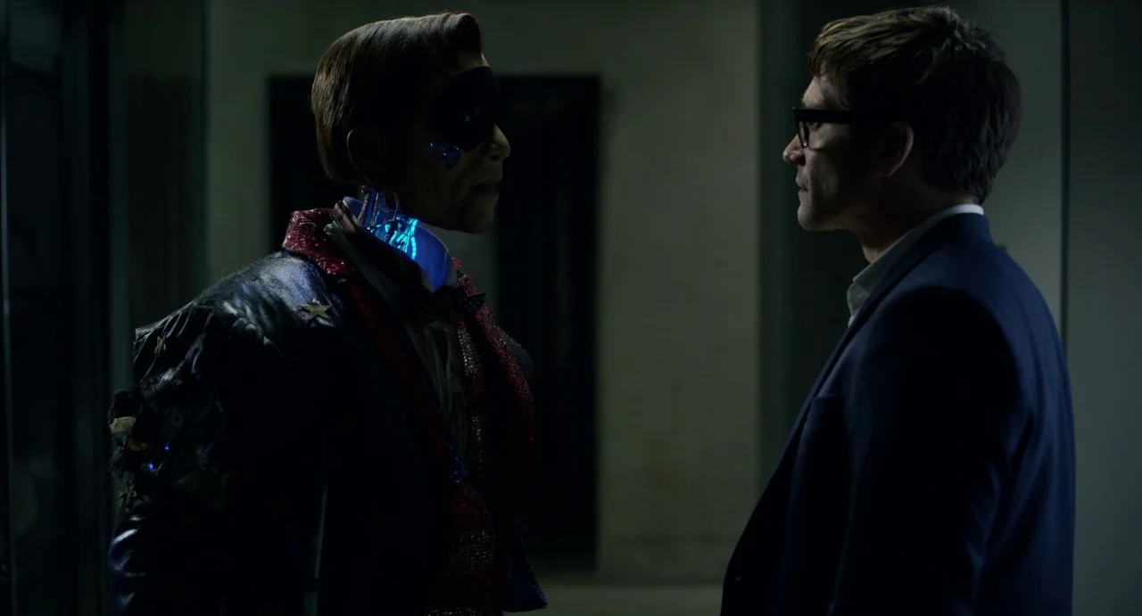 Velvet Buzzsaw (2019) movie still: medium — A dimly lit indoor hallway with a blurred dark background. A man wearing a mask and a mechanical neck…