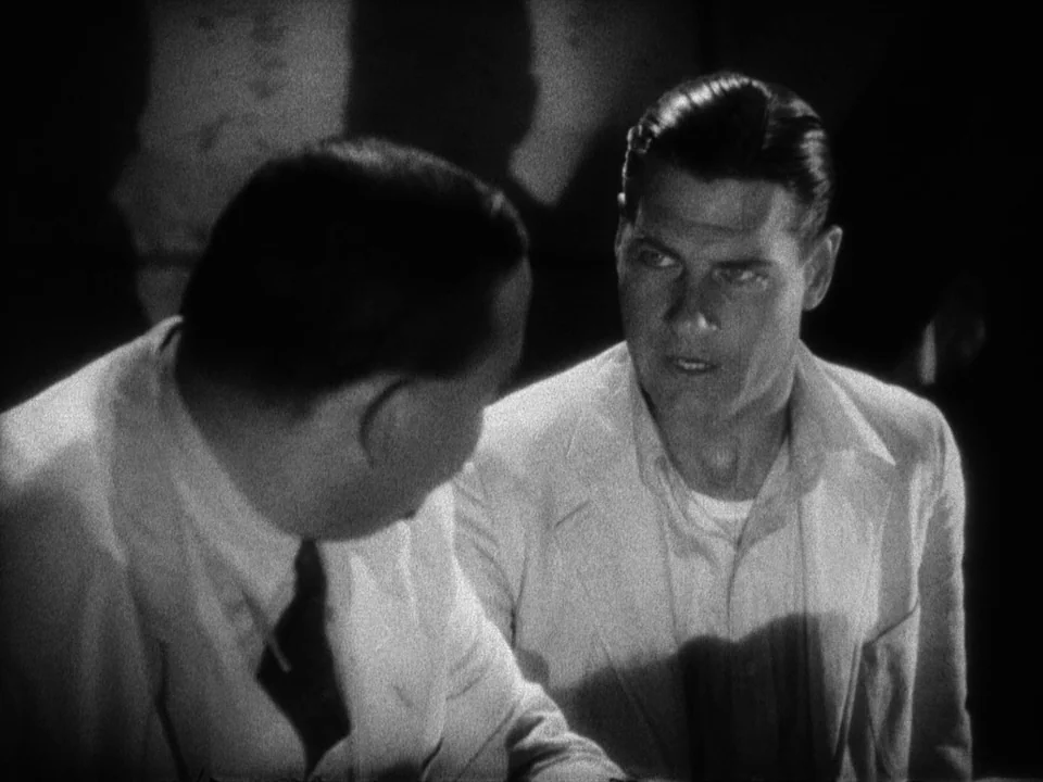 Island of Lost Souls (1932) movie still: medium — A dimly lit room features two men sitting across from each other in suits. The man on the right…
