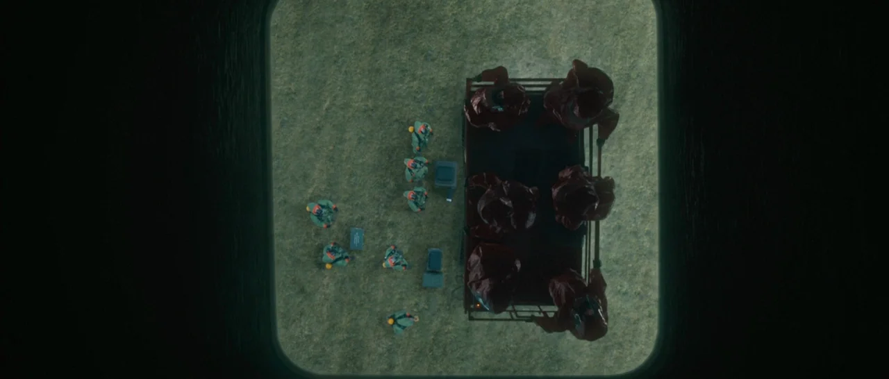 Arrival (2016) movie still: wide — An overhead view of a green grass field with a small flatbed truck parked. Several individuals wearing red and…