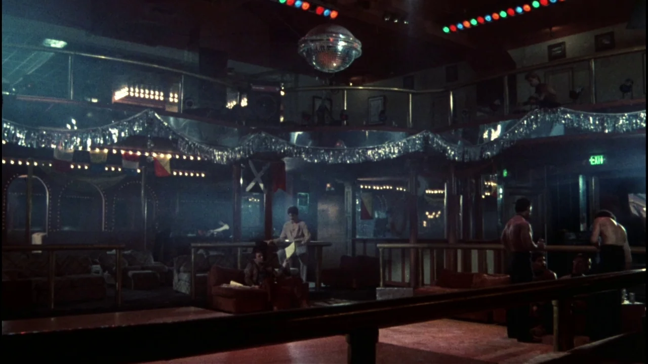 Star 80 (1983) movie still: wide — A dimly lit 1980s nightclub interior features tiered seating, mirrors, and silver tinsel decorations. Groups of…