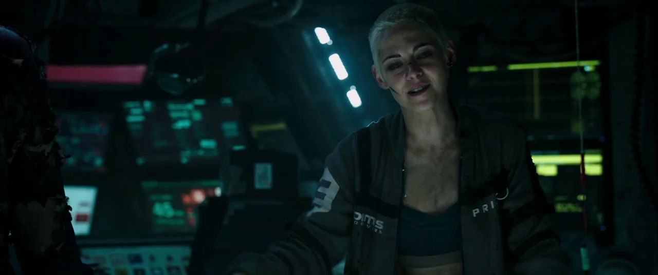 Underwater (2020) movie still: medium — A dimly lit, high-tech compartment features glowing monitors and complex control machinery. A woman with a…