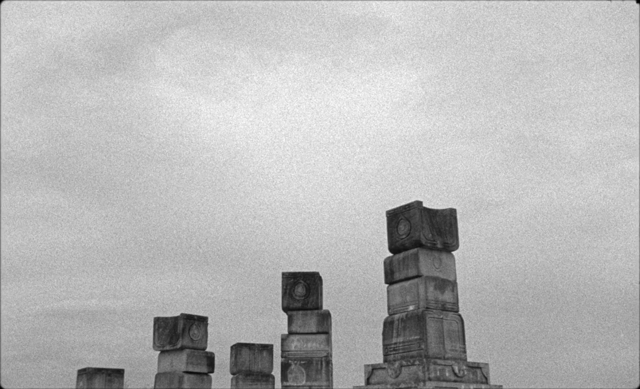 Last and First Men (2020) movie still: wide — A series of stone pillars stand against an overcast sky. The structures feature carved geometric…