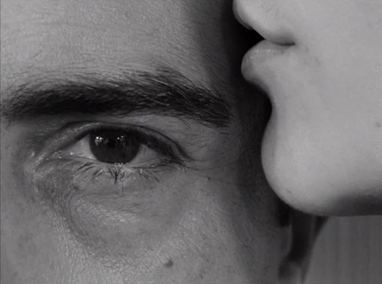 Une Femme Mariée (1964) movie still: closeup — An extreme close-up focuses on the side of a man's face and a woman's lips. The woman rests her mouth…